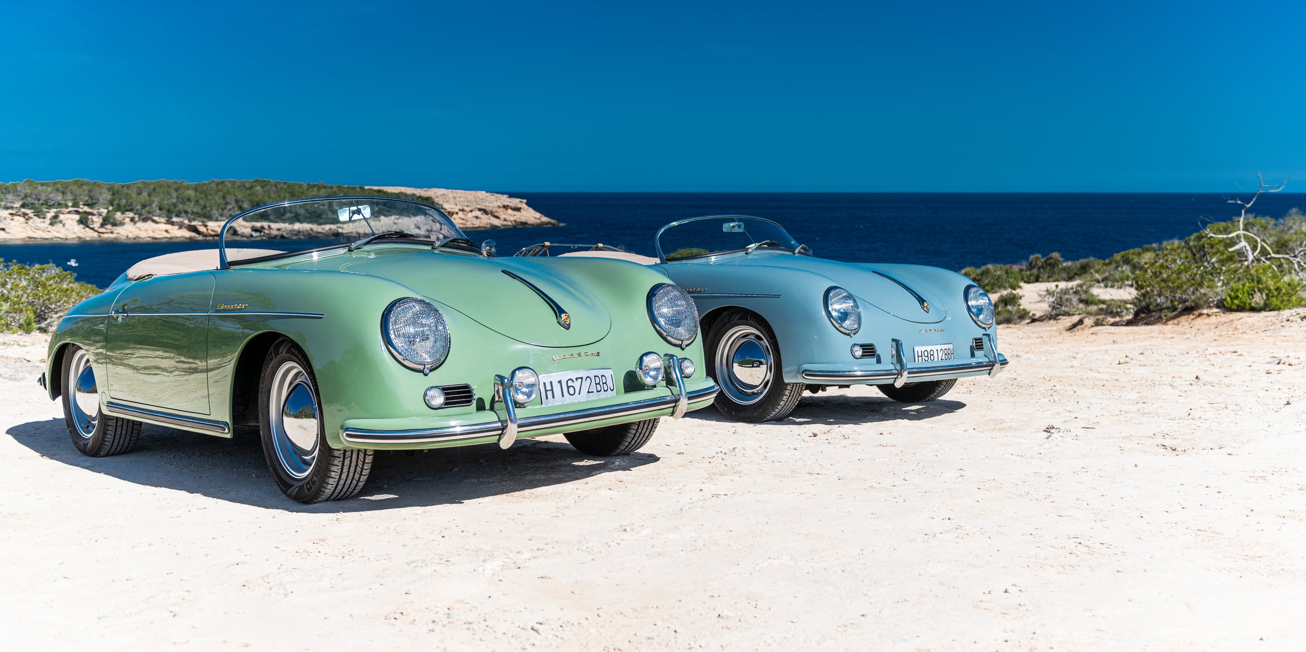 A light-blue Porsche 356 Speedster on the beach, with the sea and the Ibiza coast behind it.